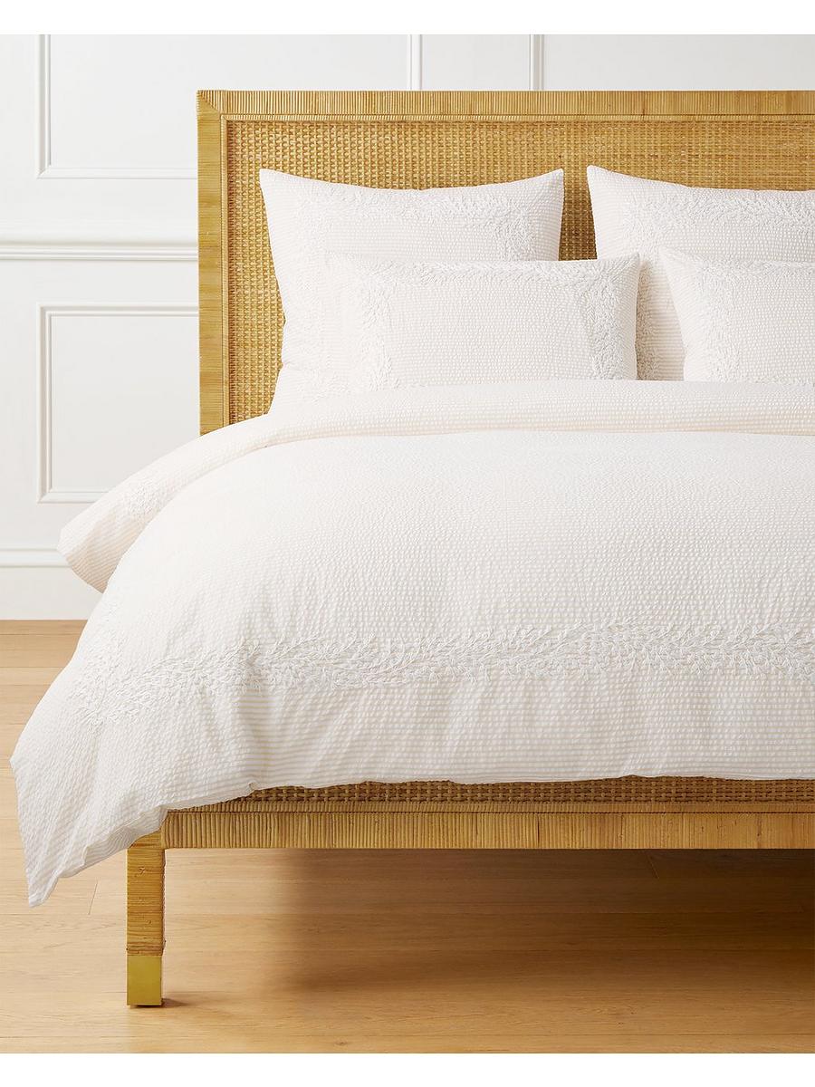 Sand seersucker duvet and shams with embroidered cream trim on a rattan bed